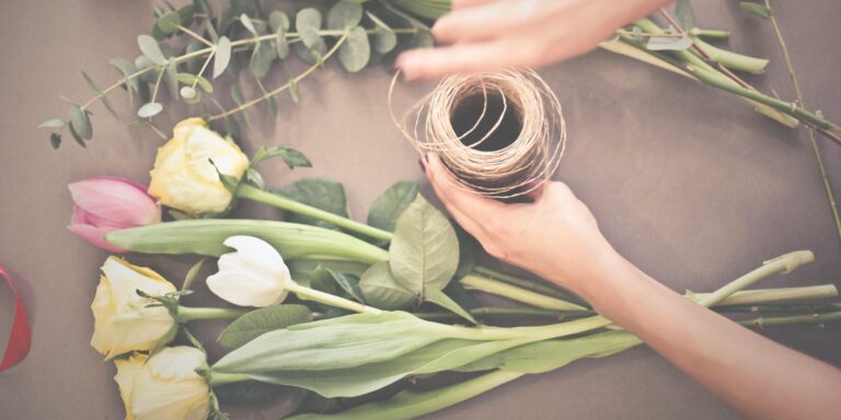 Florists table with small bunch of tulips and stem of eucalyptus. Hands above bench uncurling florists string. Floristry workshops, wedding flowers & gifts