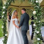 bride & groom with flower garland around bridal arch