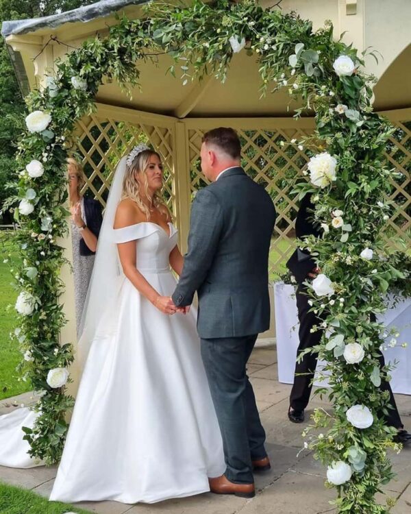 bride & groom with flower garland around bridal arch